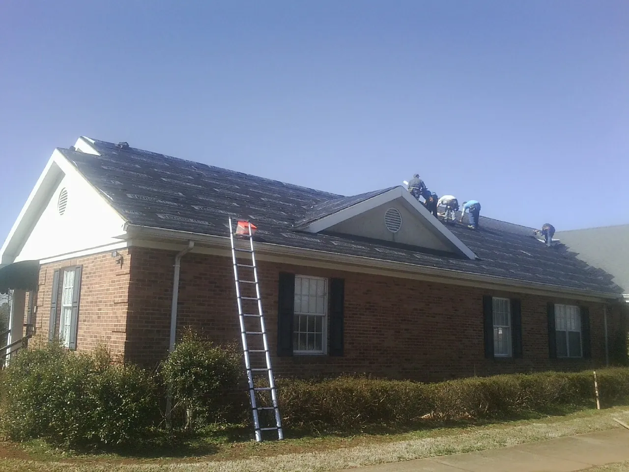 Crew tearing shingles off a brick ranch roof with a ladder set — Metal Roof Repair work by our crew in Hoosick Falls