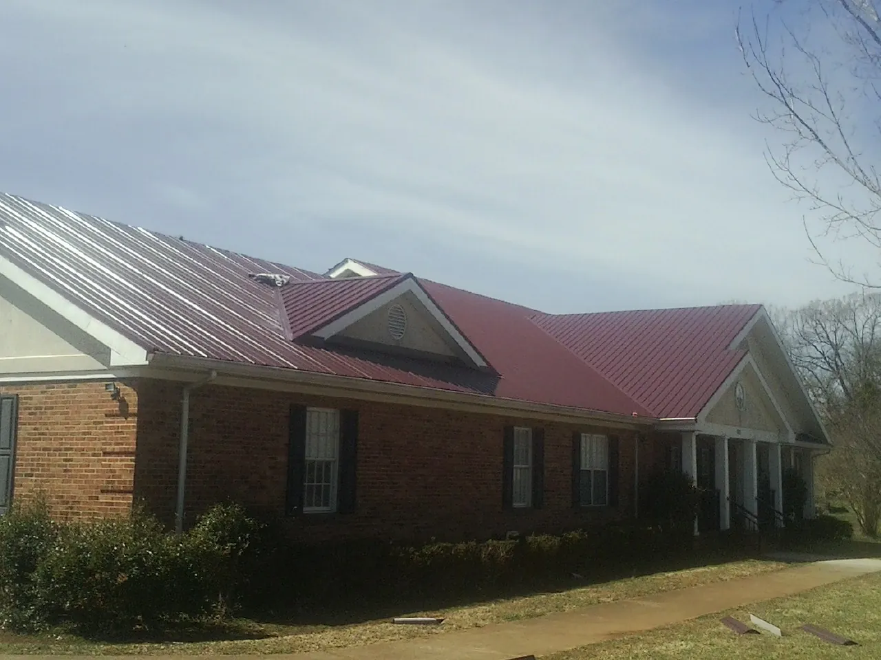 Red metal roof with gabled entries on a long brick building, from a Hail Damage Roof Repair job in Hoosick Falls