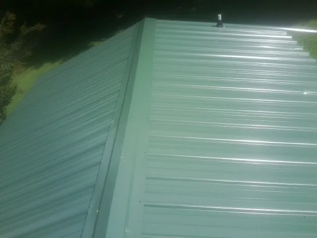 New green metal panels meeting at the ridge of a roof — Flat Roof Repair work by our crew in Hoosick Falls
