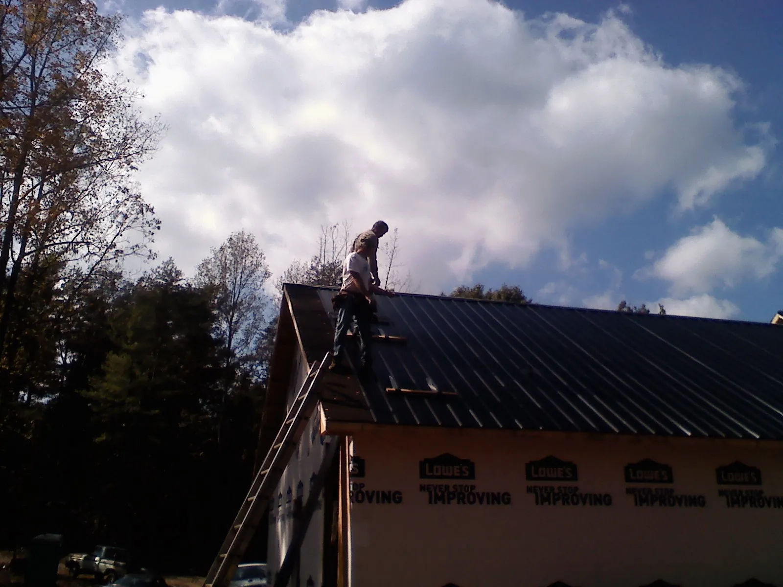 Roofer fastening dark metal panels high against a cloudy sky, from a Roof Inspection job in Hoosick Falls