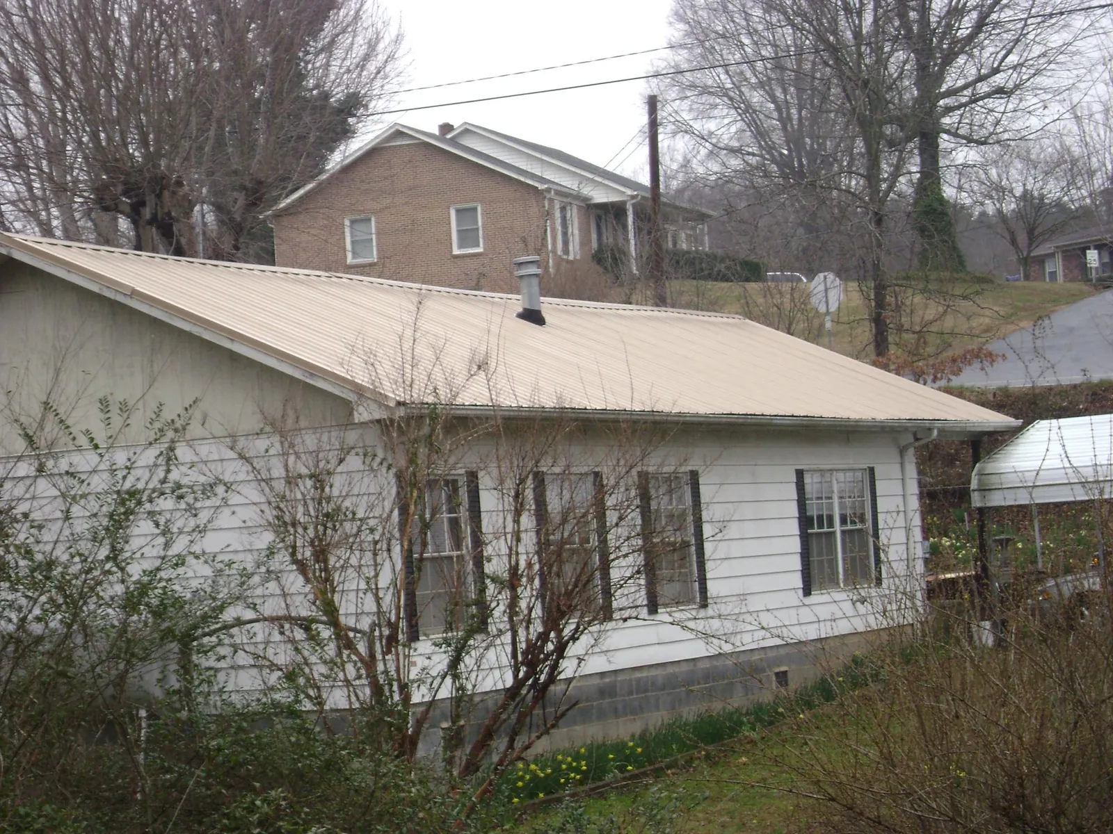 Tan metal roof on a white sided house set into a hillside — Commercial Roofing by Roofing Brothers in Hoosick Falls